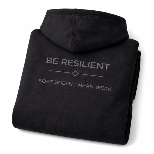 Folded Be Resilient black hoodie displaying the embroidered "Soft Doesn't Mean Weak" back design.